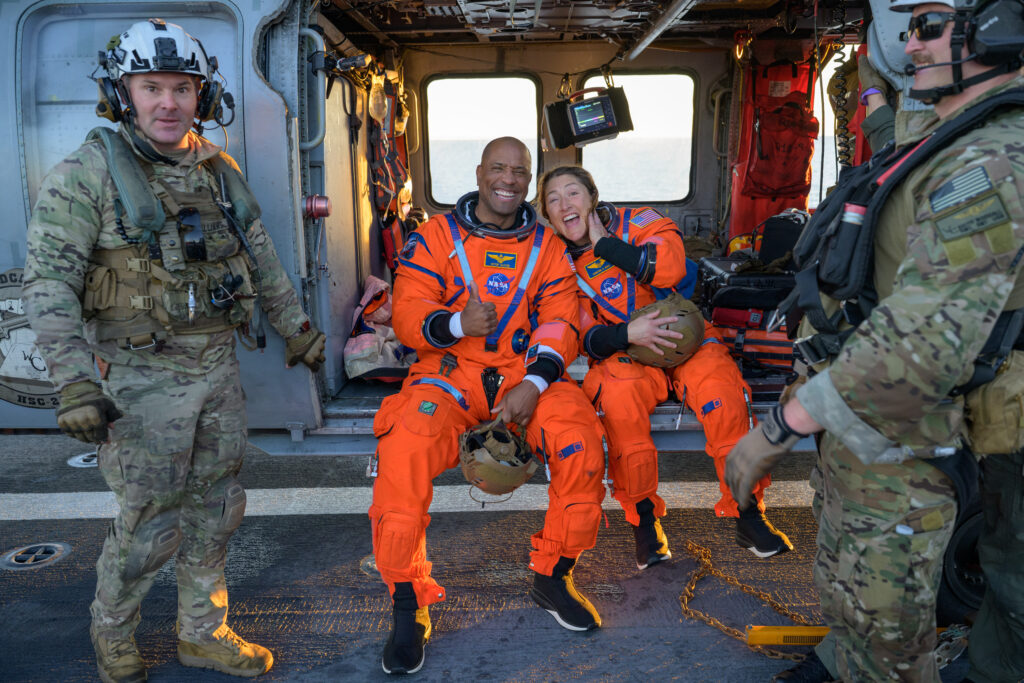 NASA astronauts Victor Glover, Artemis II pilot, left, and Christina Koch, Artemis II mission sitting on a Navy MH-60 Seahawk on the flight deck of USS John P. Murtha after they and fellow crew mates were recovered from Orion spacecraft after splashdown.
