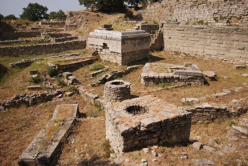 Archaeological Site of Troy (Turkey) showing ancient stone ruins with a circular well and rectangular stone structures. (Photo UNESCO)